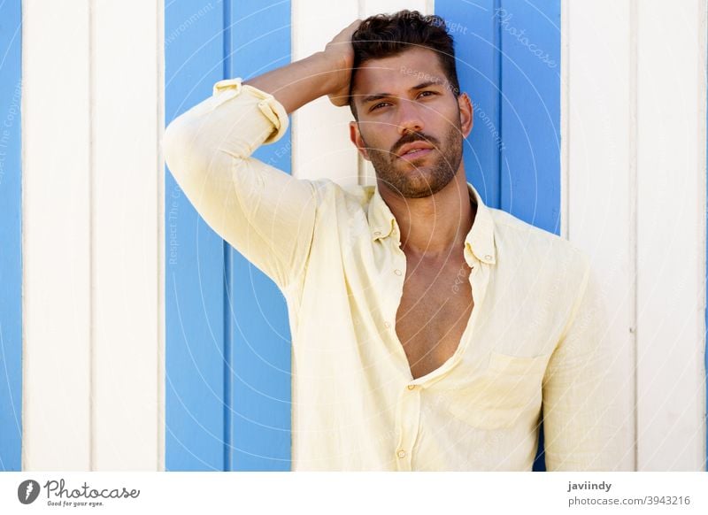 Young man, fashion model, posing in front of a beach booth. hairstyle summer fashionable beard looking person guy young shirt handsome portrait background adult