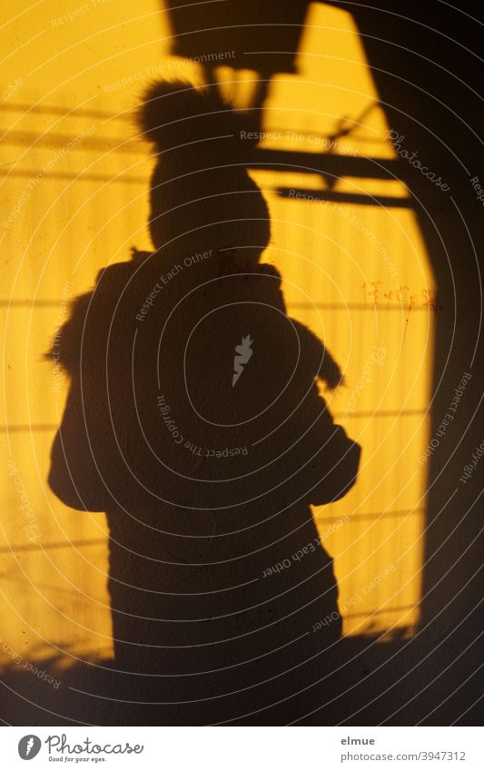 Shadow of a person with bobble hat and thick scarf on a wall / shadow play / winter Shadow play Winter Bobble hat Scarf Wall (building) Yellow Black