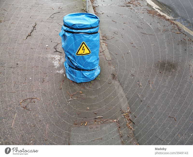 Blue plastic rain shelter with yellow warning over an electrical distribution box on the sidewalk next to a bike path in the rain stom Electricity Short-circuit