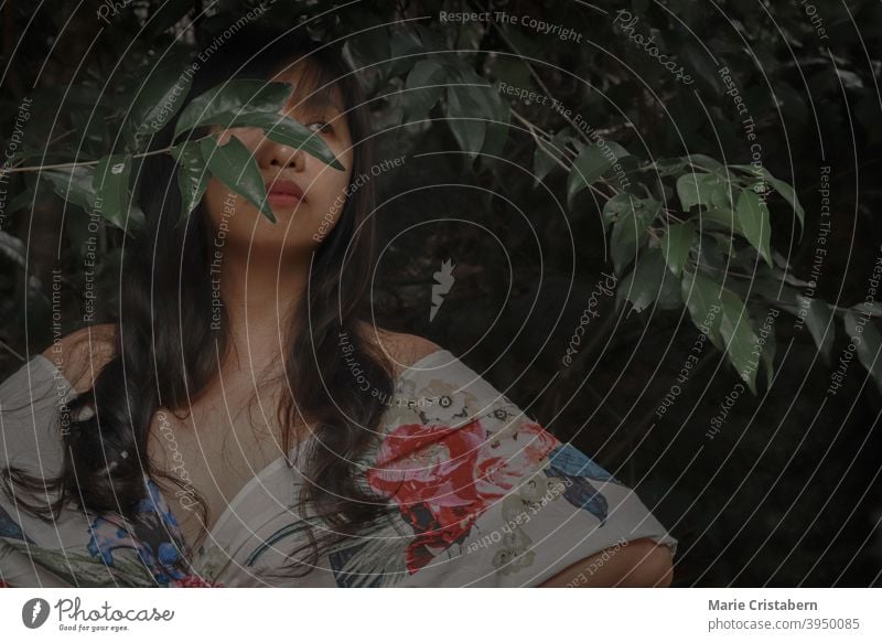 Beautiful woman in a floral dress among the dark tropical foliage sensuality elegance pretty fresh face leaves mysterious environmental summer season natural