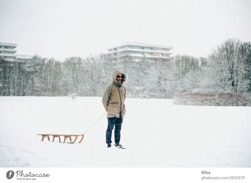 Man with sled in snow and skyscrapers in background Sleigh Snow Meadow Nature Human being sledging wood sledges Winter Winter's day Gray White Cold Snowscape