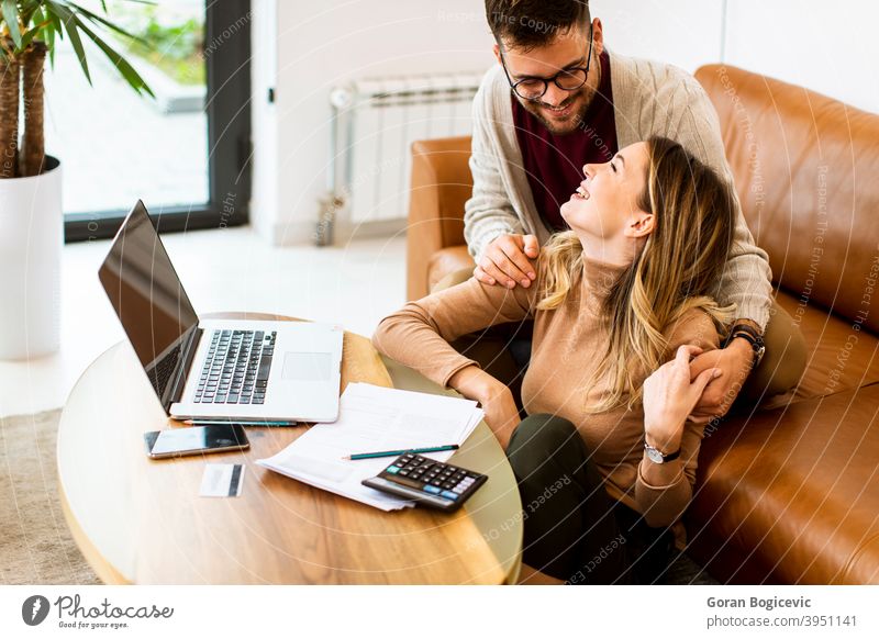 Young couple using laptop together while sitting on sofa at home woman internet happy computer indoors people caucasian couch house room young smiling lifestyle