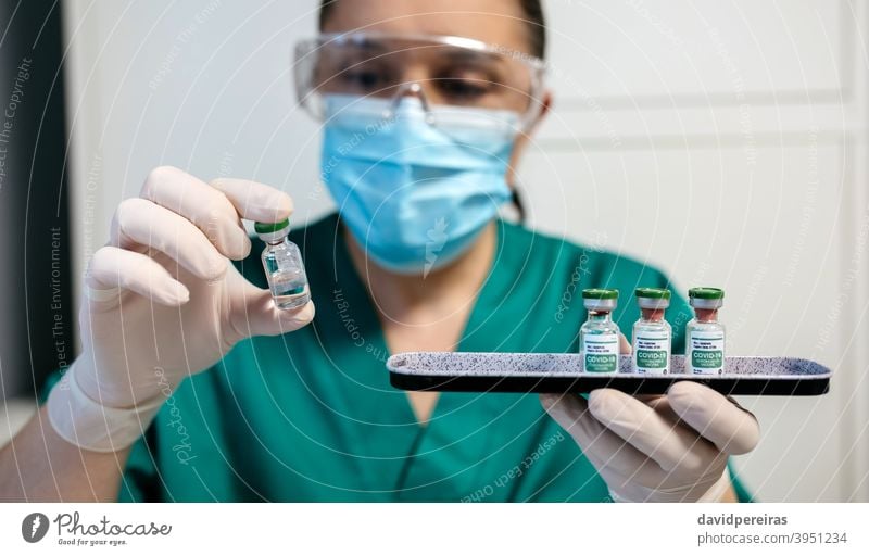 Female laboratory technician examining vial of coronavirus vaccine. pharmaceutical laboratory covid-19 tray medical medicine caution plate research drug