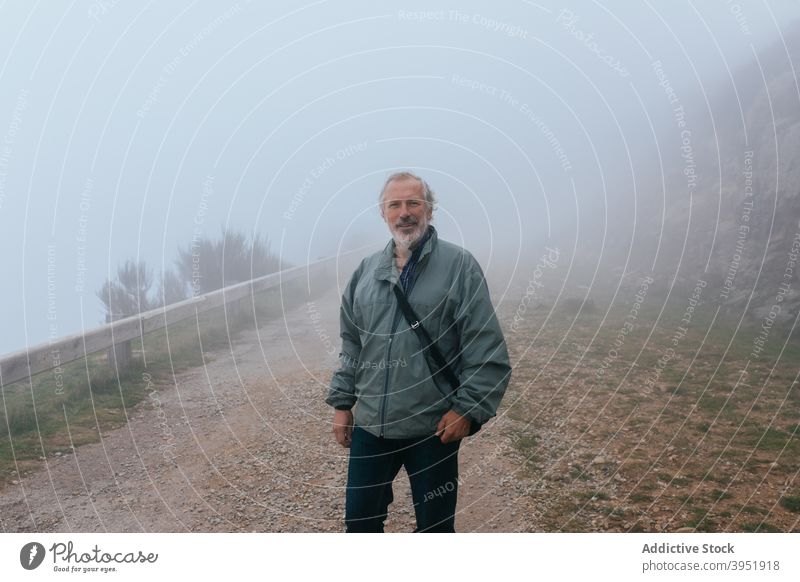 Mature man stranding on path in foggy day traveler mature nature smile mist autumn male vacation middle age trip happy haze fall weather season cheerful tourism