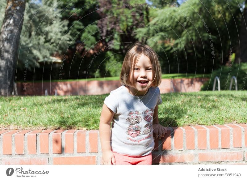 Happy cute kid resting in courtyard on sunny day child smile play happy excited nature tree joy childhood holiday positive relax girl adorable casual blond