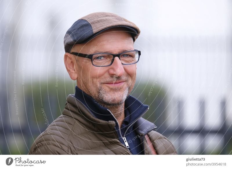 Portrait of a happy, smiling man with glasses, cap and grey three-day beard Looking into the camera Front view Upper body portrait Central perspective