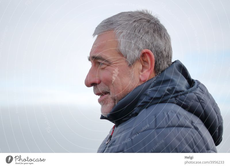 Portrait of a smiling senior citizen in profile with grey short hair, three-day beard and blue winter jacket with hood Human being Man Senior citizen masculine