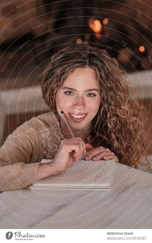 Smiling woman taking notes in notebook at home write diary fireplace cozy take note smile domestic female house content rest cottage comfort joy sit relax happy