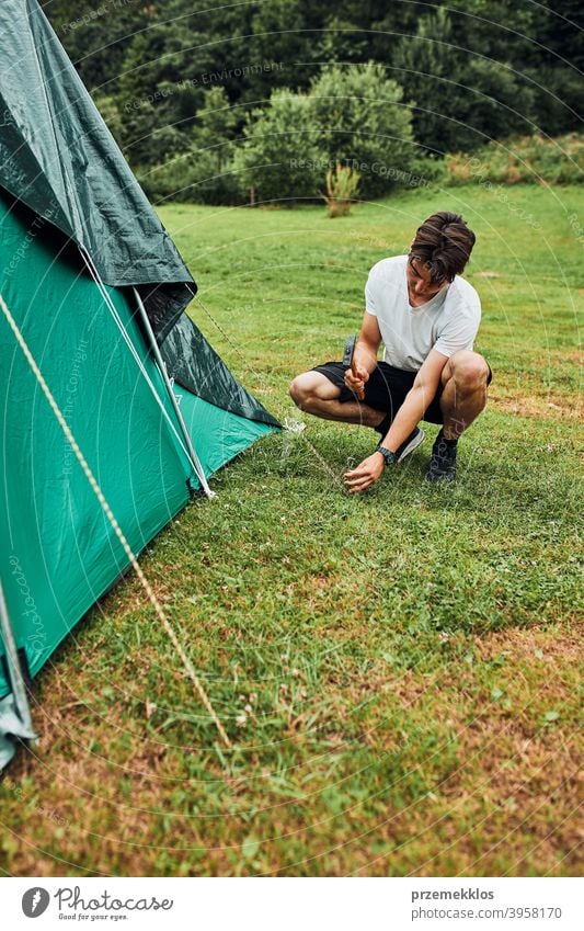 Young man putting up a tent on camping during summer vacation trip stake peg hammer grass setting pitching teenager young copy space leisure countryside person