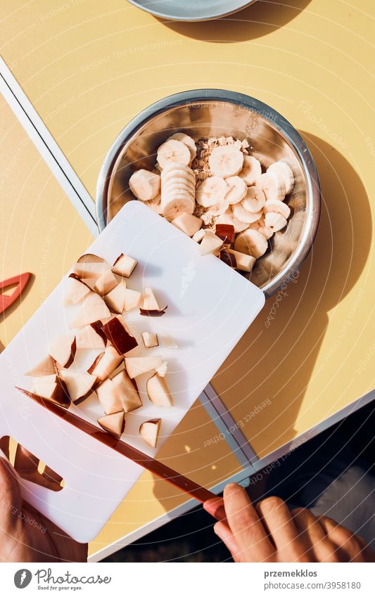 Man preparing healthy breakfast with fruits and oat flakes outdoors on camping. Close up of male hands cutting apples and bananas for breakfast table board