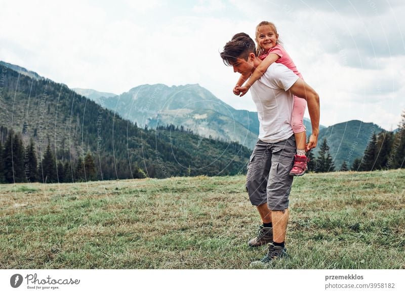 Young man holding little girl on his back. Child playing with her elder brother riding on his back enjoying summer day together happy excitement enjoyment