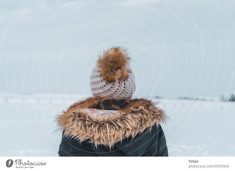 Back view of young woman with wool cap and jacket in snow Woman youthful Rear view Woolen hat Winter Snow Exterior shot Cold Loneliness Peaceful contemplating