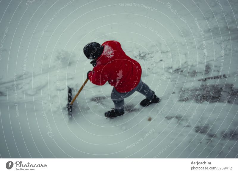 A person with a red jacket and a black cap, pushes with a snow shovel the snow laboriously and with much strength out of the way. clear snow Snow Winter Cold