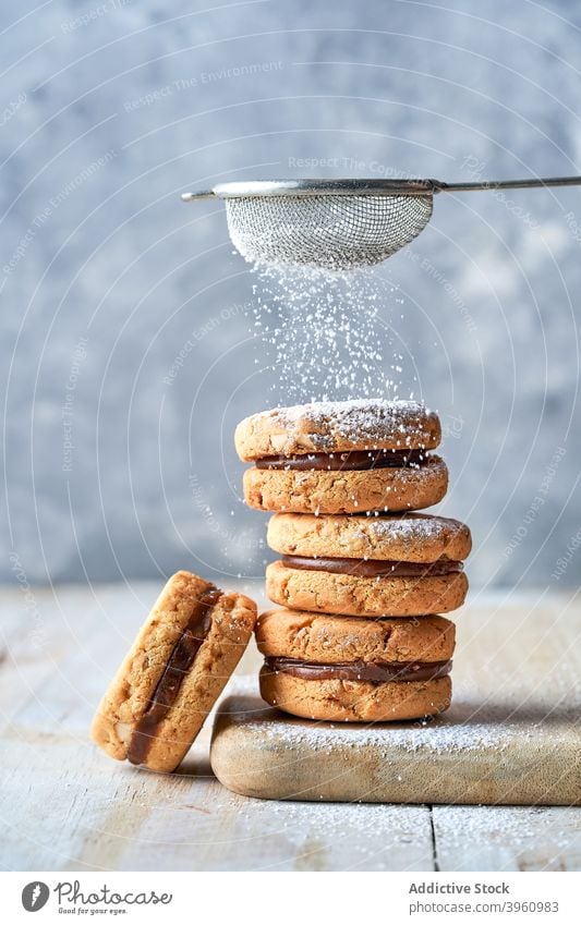 Sandwich cookies sprinkled with powdered sugar sandwich biscuit dessert sweet caramel fill pile stack heap treat food wooden cutting board chopping board table