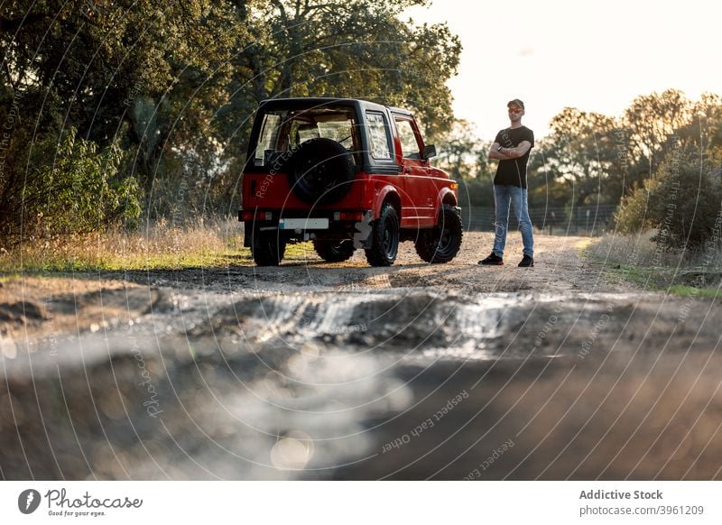 Adventurer with SUV car standing on dirt country road off road suv trace wet drive adventure nature journey travel vehicle lifestyle male summer countryside