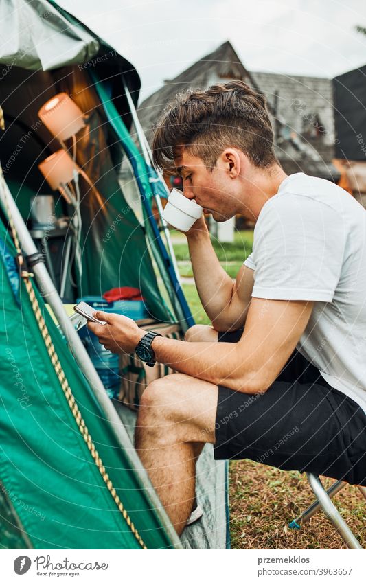 Young man drinking a coffee sitting at front of tent in the morning adventure beverage break breakfast camp camping closeup cup exploration freedom hiker hot