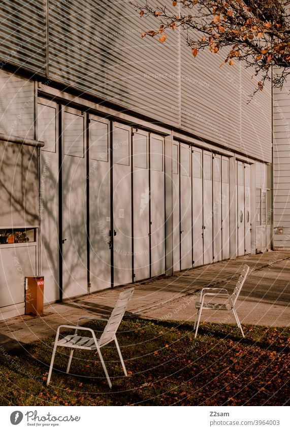 Stühle im Aussenbereich einer Industriehalle industriehalle stühle einfahrt tore produktion warme farbe pause erholung mittagspause bäume schatten licht herbst