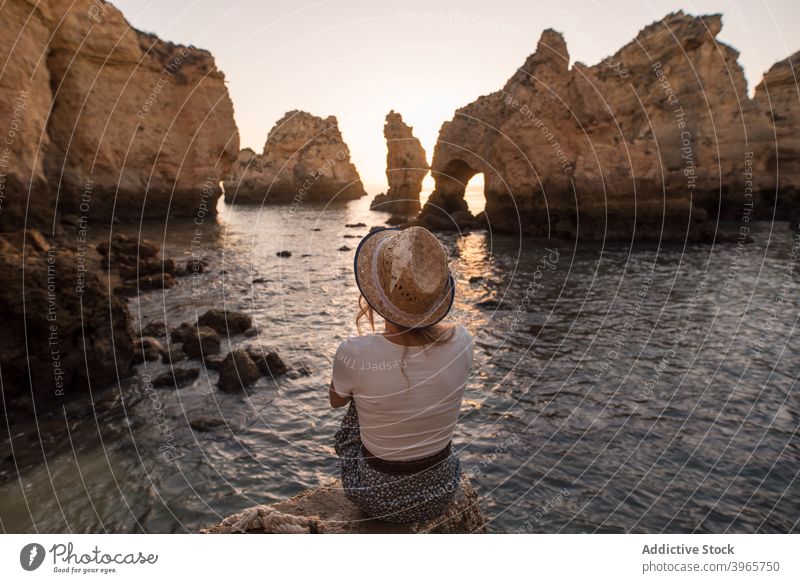 Unrecognizable woman resting near sea and cliffs admire sunset water nature coast stone algarve portugal vacation sit hat ocean travel relax idyllic evening