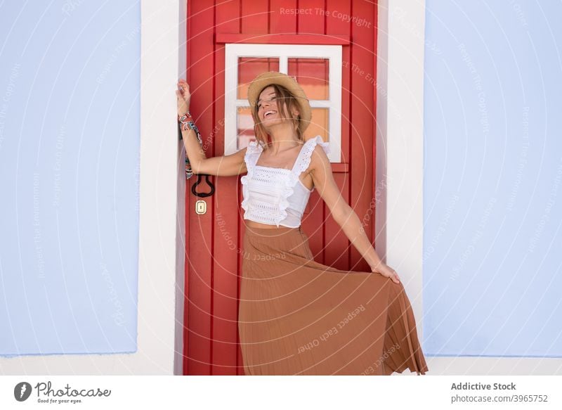 Cheerful stylish young lady standing near door of typical house on sunny day woman happy smile fashion style vacation architecture facade tourist content