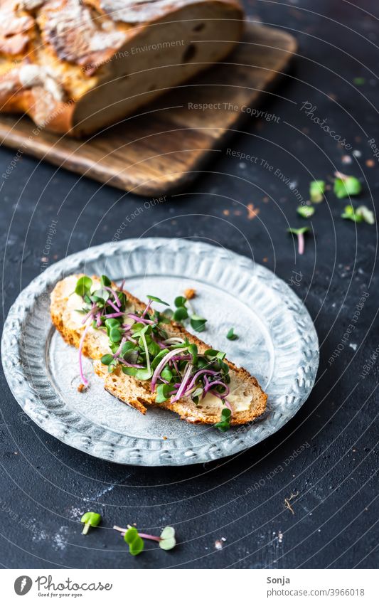 A slice of bread with cress on a rustic plate Slice of bread Cress Butter Plate Rustic Bread black background Close-up Breakfast Delicious Fresh Eating Meal