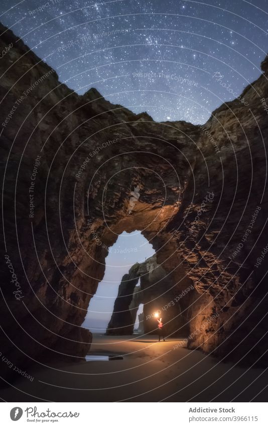 Traveler with flashlight near rocky arch under night sky starry traveler beach seashore dark glow explorer milky way breathtaking scenic seaside picturesque