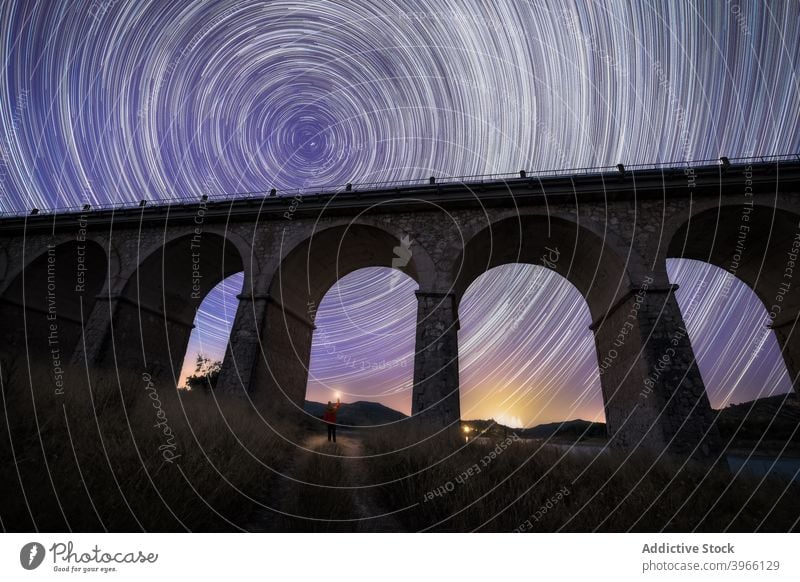 Traveler under bridge and night starry sky traveler viaduct spectacular trail circle move galaxy landscape dark glow illuminate flashlight sparkle dusk