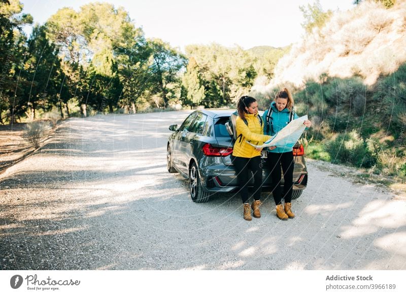 Female travelers navigating with map on road women navigate read car search orientate route female direction together paper journey tourism trip guide stand