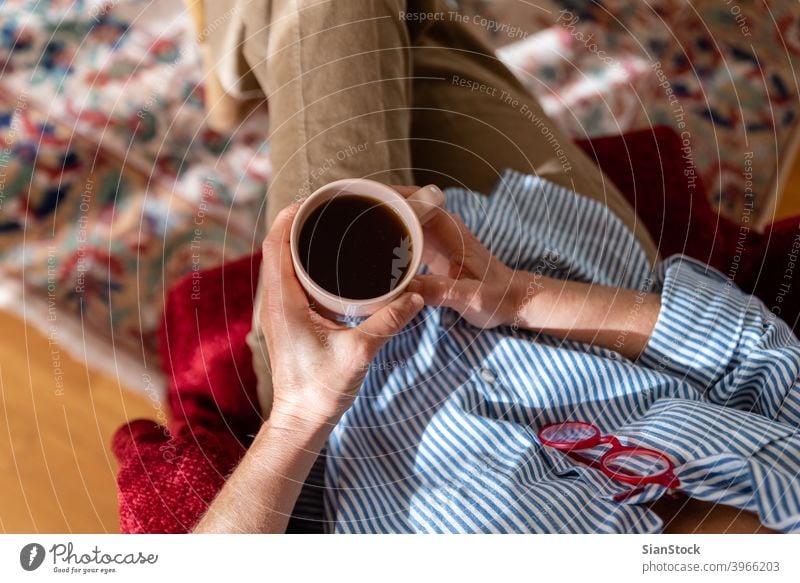 Hands of mature woman holding cup of coffee, top view room watching communication leisure hands older red glasses armchair carpet elegant grandmother senior