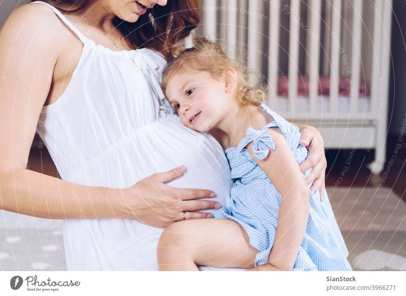 Girl listening to her pregnant mother's belly girl daughter ear home room brother coming mom child playing brunette blonde pink family baby person female