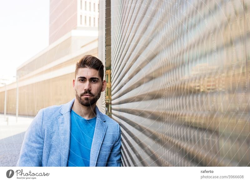 Young bearded man in urban background wearing casual clothes while leaning on a wall and looking at camera cool style portrait guy 1 photogenic stylish modern