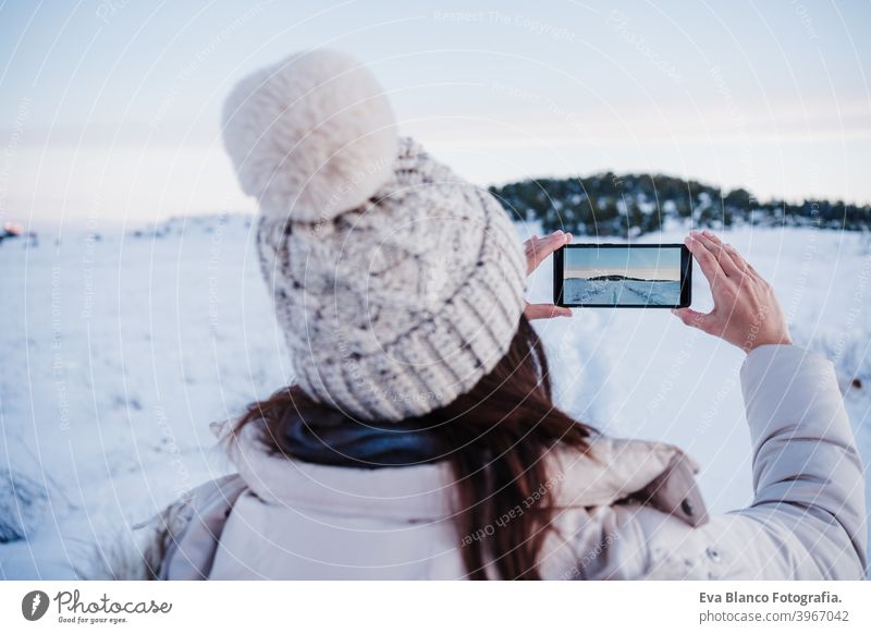 back view of backpacker woman hiking in snowy mountain taking a picture of landscape with mobile phone.winter season. nature and technology sunset cold covered