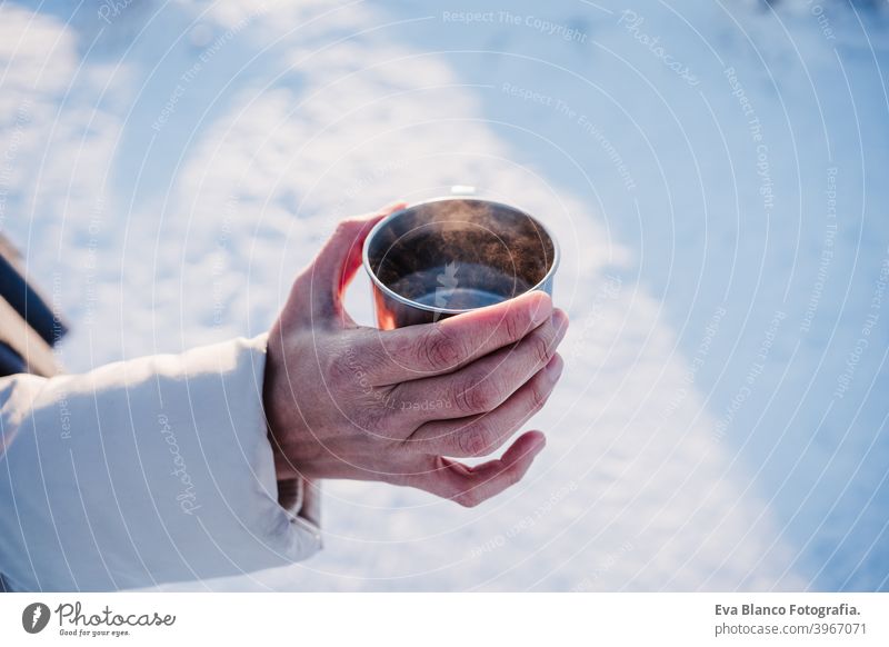 unrecognizable young woman at sunset in snowy mountain holding a cup of hot tea. Travel and Nature concept. winter season thermos drink hot water sunny hiking