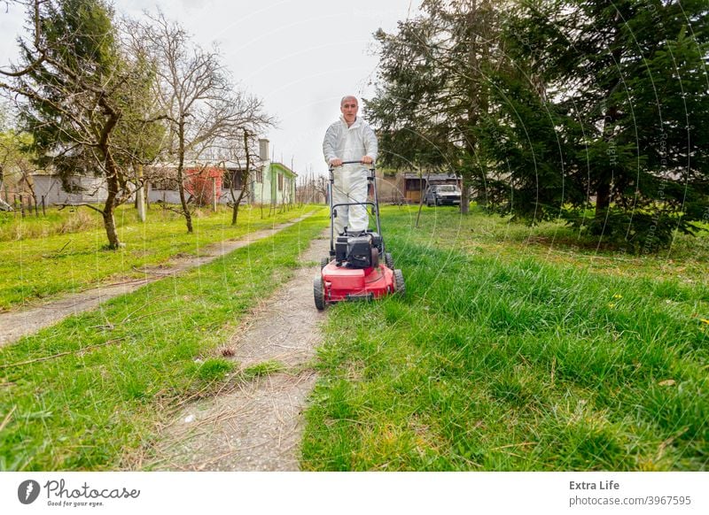 Farmer in protective clothing is mowing a lawn in a garden with a petrol lawn mower Backyard Bloom Botanic Botanical Care Clipper Cultivate Cut Cutter Early