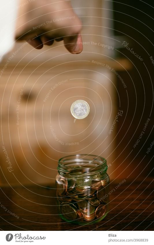 A hand throws a euro into a jar full of coins. Saving. Coin Save Money Hand Bird's-eye view Glass Money box Euro Loose change Coins stop small livestock