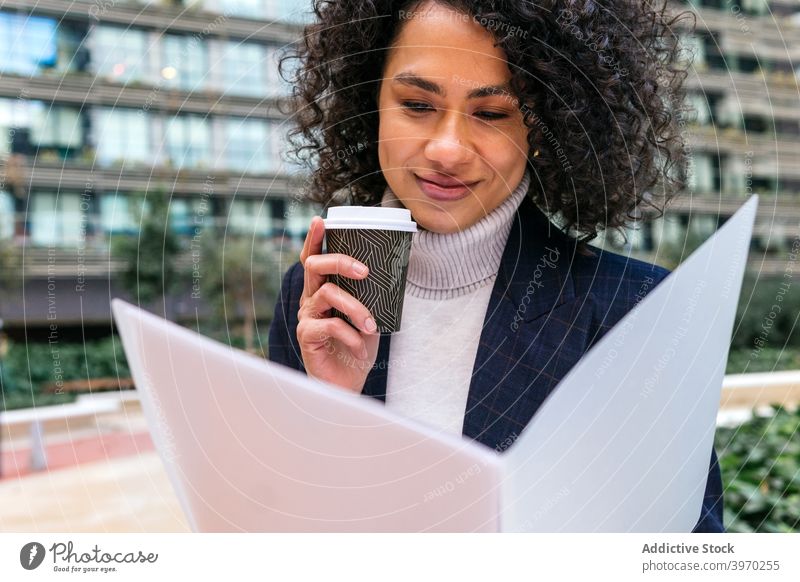 Ethnic businesswoman reading documents and drinking coffee in street takeaway city smile entrepreneur to go paper female ethnic black african american cup urban