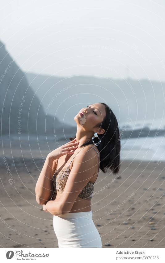 Sensual ethnic woman standing on sandy beach sensual enjoy style fashion slim young elegant summer asian female allure sunlight trendy relax beautiful harmony