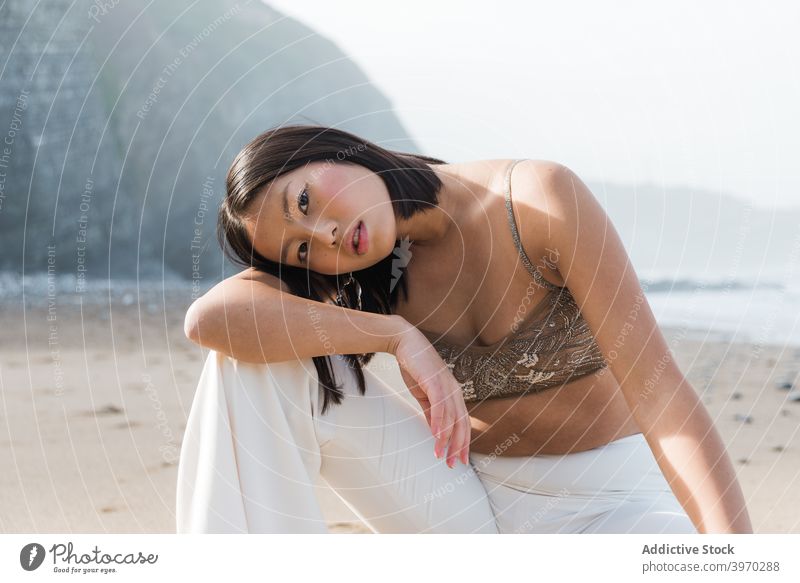 Dreamy ethnic woman in stylish outfit resting on beach fashion style sensual dreamy elegant relax serene young asian female seashore coast lifestyle ocean lady