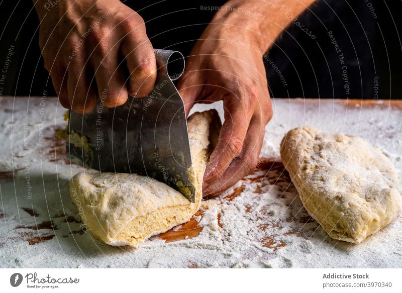 Crop baker with bread dough on floured table divide raw bakery man ball scraper separate knead bakehouse process gourmet loaf chef culinary gastronomy artisan