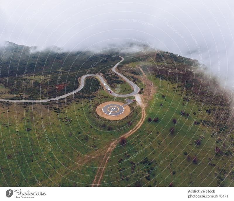 Modern round helipad in green suburbs road curve mountain landscape highland picturesque terrain nature scenery scenic hill valley idyllic destination