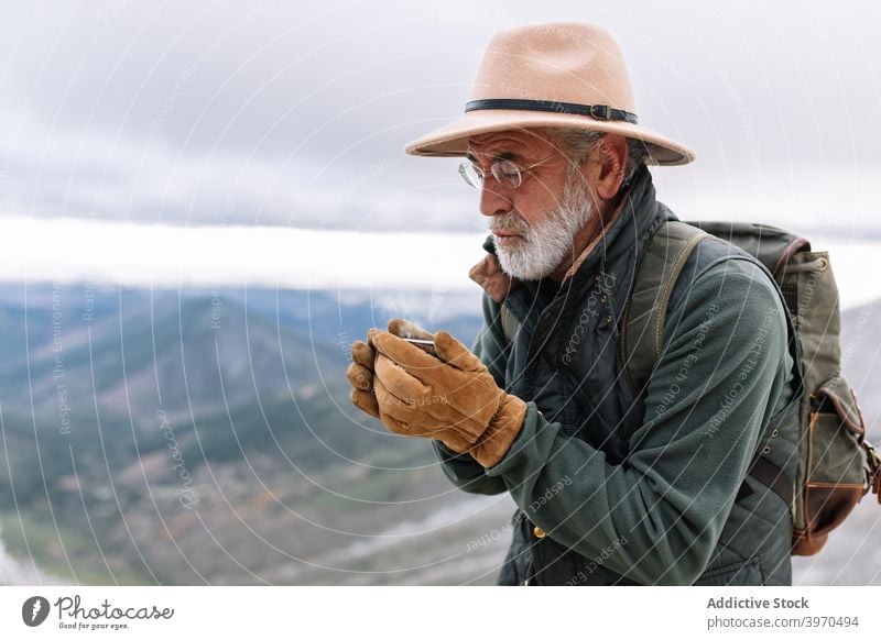 Senior traveler drinking hot coffee in highlands man pour mountain winter senior male caceres extremadura spain outerwear hiker elderly beverage cold cup