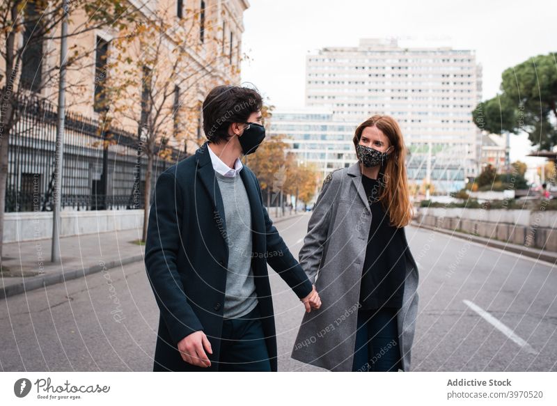 Young couple in protective masks walking on city street urban happy together holding hands coronavirus new normal love relationship romantic young lifestyle