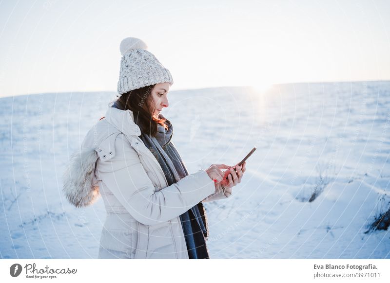 beautiful young woman at sunset in snowy mountain using mobile phone. Nature and technology concept. winter season hiking cold covered caucasian forest