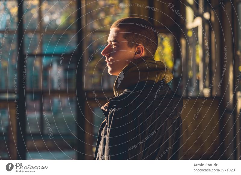 portrait of a young man in profile with evening sun sunlight hoodie frame building ruin sunset calm silent relax look standing trees nature construction sunbeam