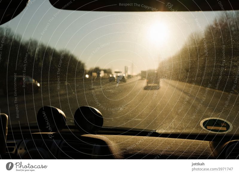 Through the dirty windshield of a car you can see the highway and the blinding sun Highway Driving In transit mobile Mobility road trip Car Street Transport