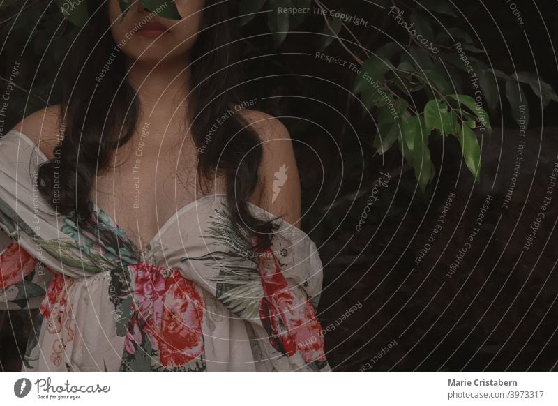 A woman wearing an off shoulder floral dress against a dark and moody tropical foliage background artistic springtime freshness concept wellness tranquility