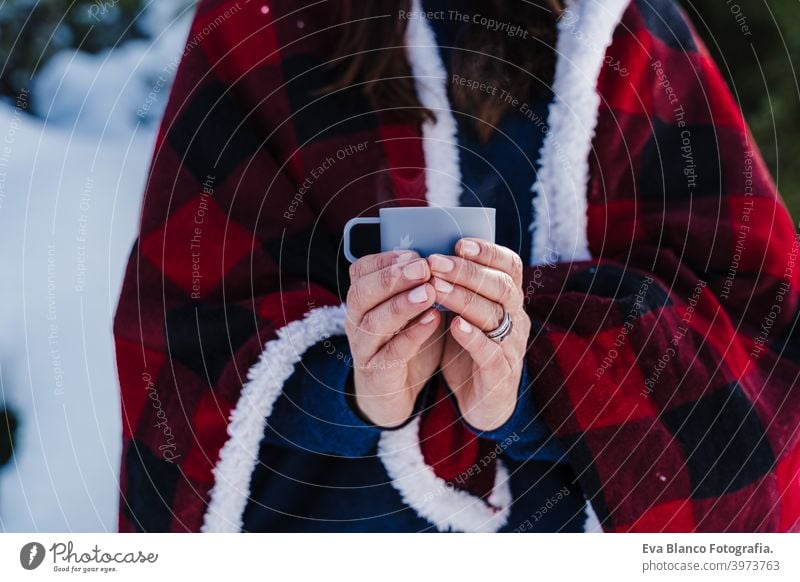 beautiful woman wrapped in plaid blanket holding a cup of hot coffee. nature and lifestyle snow mountain hot tea thermos drink sunny hiking winter cold covered