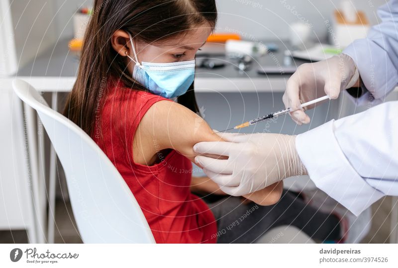 Girl receiving coronavirus vaccine at doctor's office injecting covid-19 little girl syringe injection vaccination kid child priority group arm protective mask