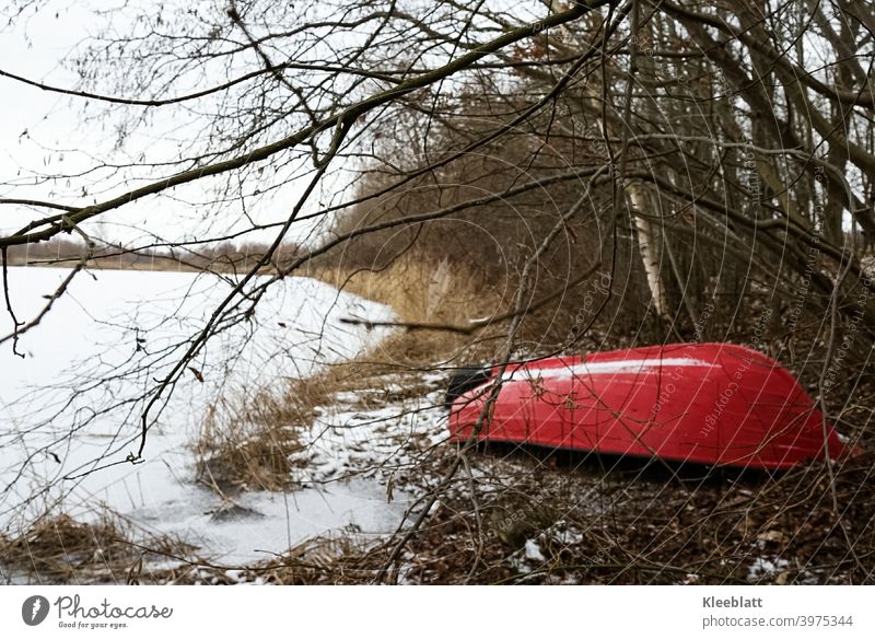 Half-hidden red boat lying on the shore waiting for spring - the lake is frozen over Red boat, See, Watercraft bank frozen lake canoe Relaxation bare trees