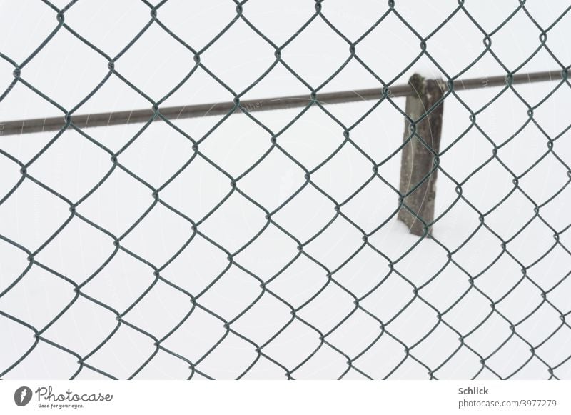 At the edge of a sports field in winter with wire mesh fence and barrier for spectators Sporting grounds Snow Chain link fence demarcation Deserted snow surface