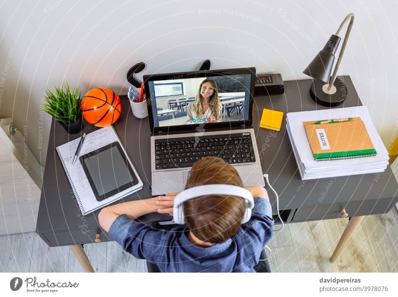 Top view of unrecognizable boy with headphones receiving class at home with laptop top view teenager teacher school at home video call desk home schooling